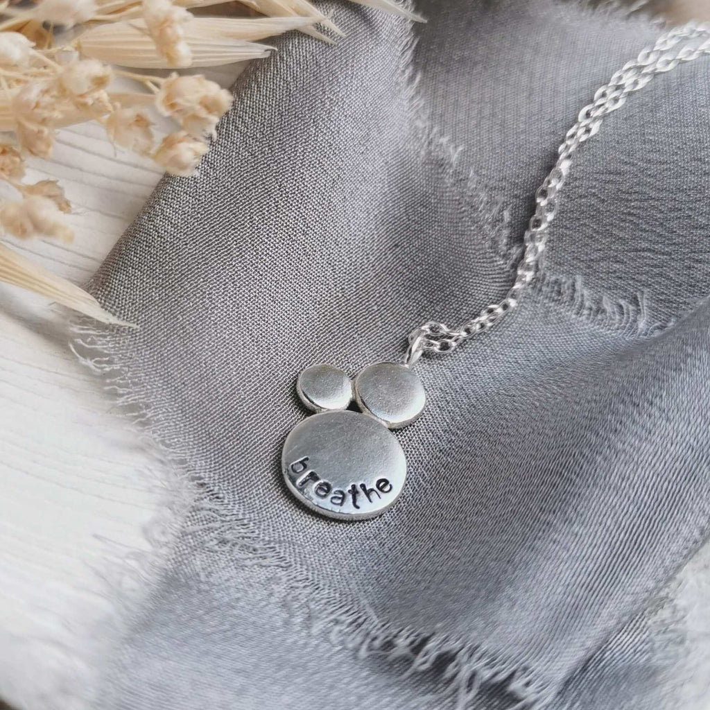 Silver necklace with 'breathe' stamped into the surface, on a textured fabric background