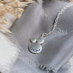 Silver necklace with 'breathe' stamped into the surface, on a textured fabric background
