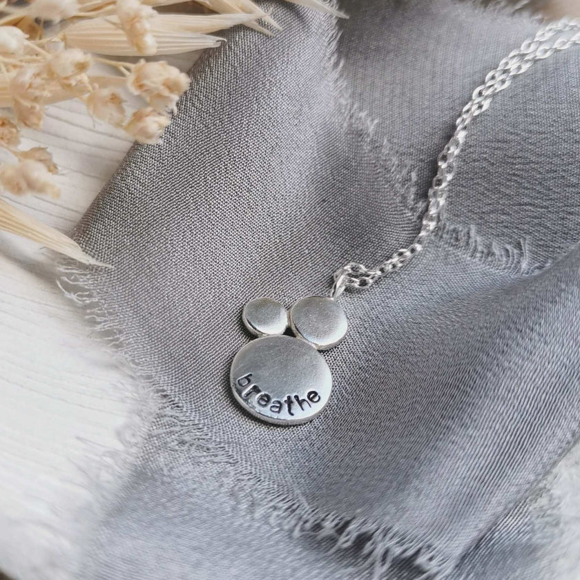 Silver necklace with 'breathe' stamped into the surface, on a textured fabric background