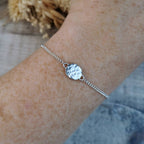 A delicate silver chain bracelet with a hammered circle disc charm, with a secret affirmation message hidden behind.  It is shown worn on a person's wrist.