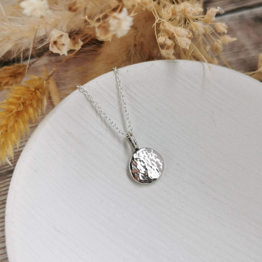 Silver necklace with a textured pendant on a white plate with dried flowers in the background