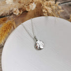 Silver necklace with a textured pendant on a white plate with dried flowers in the background