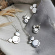 Silver jewelry mini mantra set with necklaces and earrings, all with words of affirmations stamped on them, laid on a textured surface