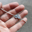 Silver bracelet with 'dare' charm held in a hand against a neutral background