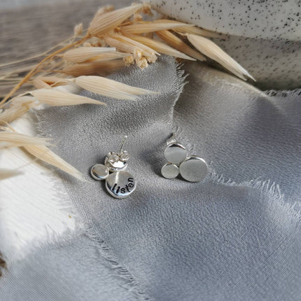 Silver earrings with a hidden word 'listen' on a textured fabric surface with dried grasses