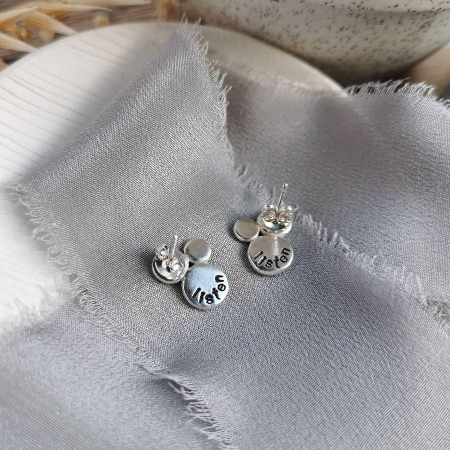 Silver earrings with hand stamped text as a personal mantra on a textured fabric surface