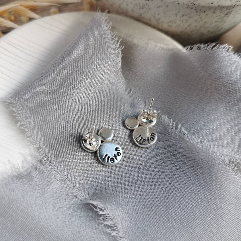 Silver earrings with hand stamped text as a personal mantra on a textured fabric surface