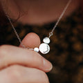 Silver necklace with round circles of silver with the word breathe stamped on, held by a hand against a blurred background
