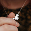 Silver necklace with round circles of silver with the word breathe stamped on, held by a hand against a blurred background