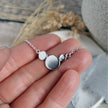 Silver necklace made of circles of recycled silver held in fingers against a blurred natural background