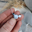 Silver necklace with round silver circles with the word Breathe stamped on, held over a blurred natural background
