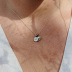 A close-up of a person wearing a delicate silver chain necklace with three small round silver charms, including one stamped with 'I can'.