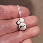 Silver pendant necklace with the custom mantra of 'rise' stamped on, held on a hand against a blurred background