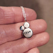Silver pendant necklace with the custom mantra of 'rise' stamped on, held on a hand against a blurred background