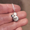 Silver pendant necklace with the custom mantra of 'rise' stamped on, held on a hand against a blurred background