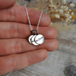 Silver necklace with round charm pendants each with a single word mantra etched into them, held in a hand against a blurred natural background
