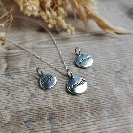 Silver charms with positive affirmations stamped into the fronts, on a wooden surface