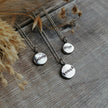 Three silver necklaces with hand stamped charms with positive affirmations of believe, align & enough on a wooden surface with dried grasses