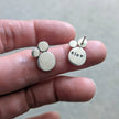 Silver earrings with 'slow' engraved on the reverse as a secret message, held on a finger against a neutral background
