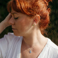 A close-up lifestyle shot of a woman with red hair wearing a delicate silver mini mantra 'breathe' affirmation necklace and matching stud earrings.