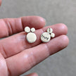 Small silver earrings with 'trust' stamped on the reverse, held on a hand against a neutral background