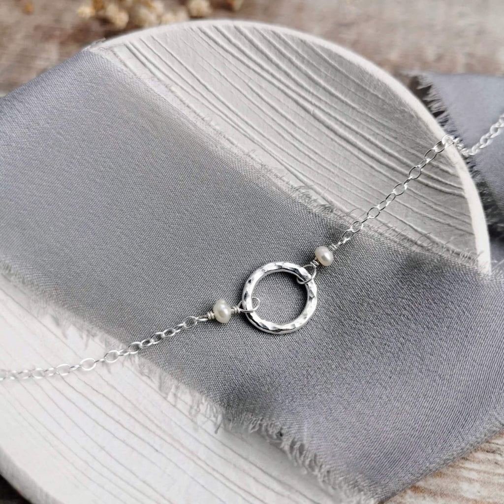 Silver and pearl necklace with a hammered circular pendant on a gray fabric surface