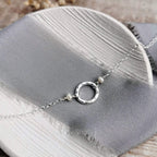 Silver and pearl necklace with a hammered circular pendant on a gray fabric surface