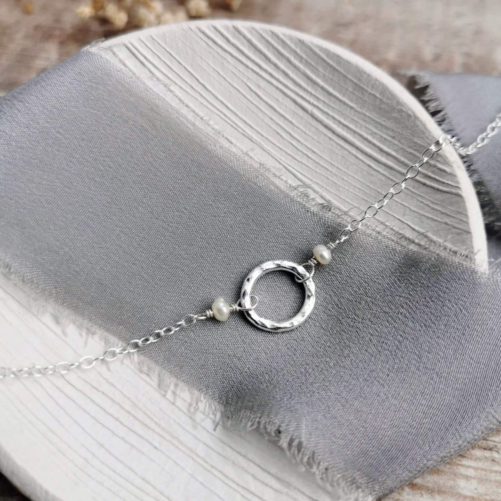Silver and pearl necklace with a hammered circular pendant on a gray fabric surface