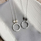 Two hammered silver circle necklaces with pearl details on a gray fabric background