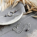Silver and black pearl necklace with extender chain on a grey surface with dried plants.