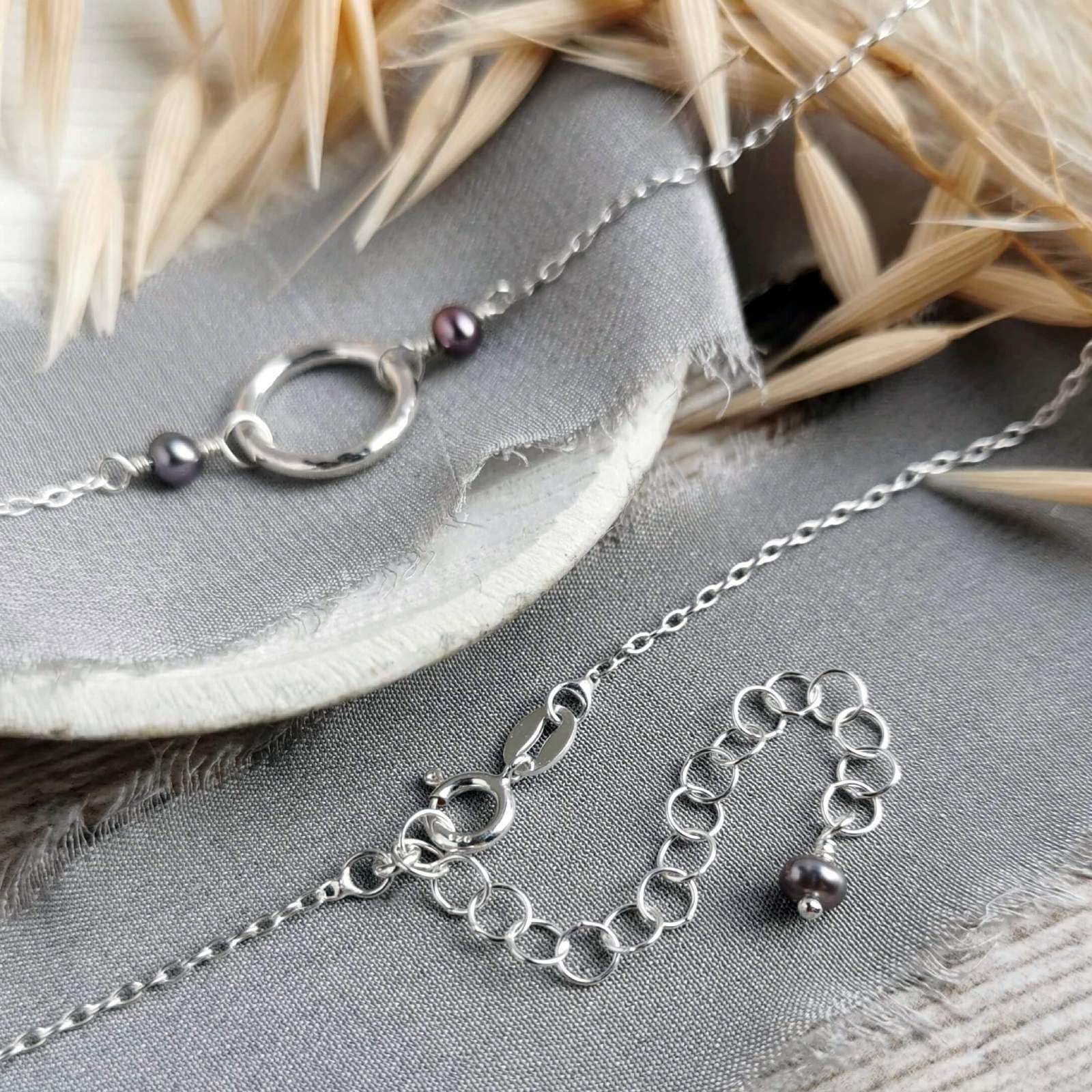 Silver and black pearl necklace with extender chain on a grey surface with dried plants.