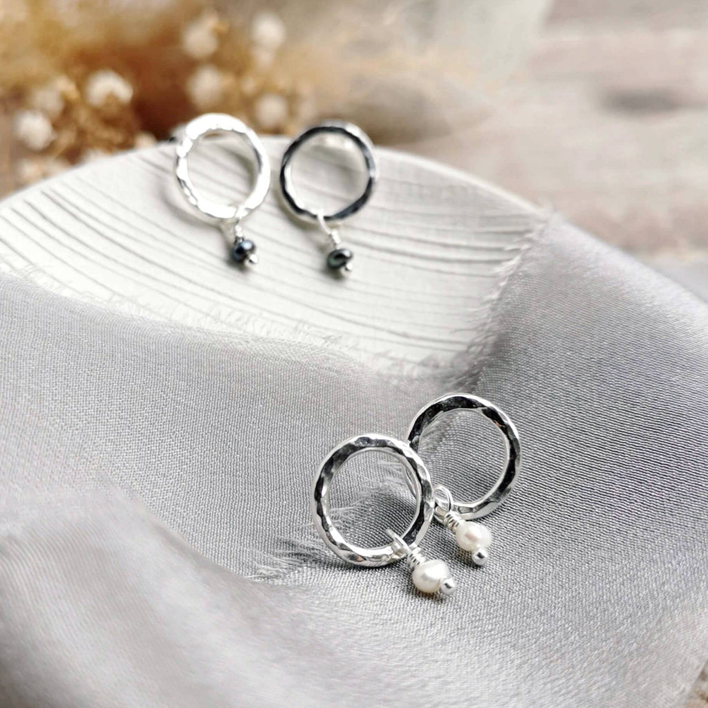 hammered Silver studs earrings with pearl drops on a soft fabric background