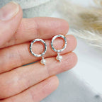 handmade Silver studs with pearl drops held between fingers against a blurred background