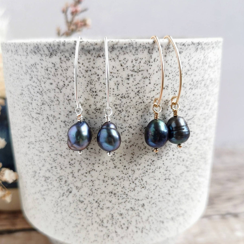 Two pairs of peacock baroque pearl earrings in silver and 14k gold fill on a speckled ceramic surface.
