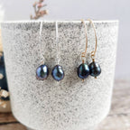 Two pairs of peacock baroque pearl earrings in silver and 14k gold fill on a speckled ceramic surface.