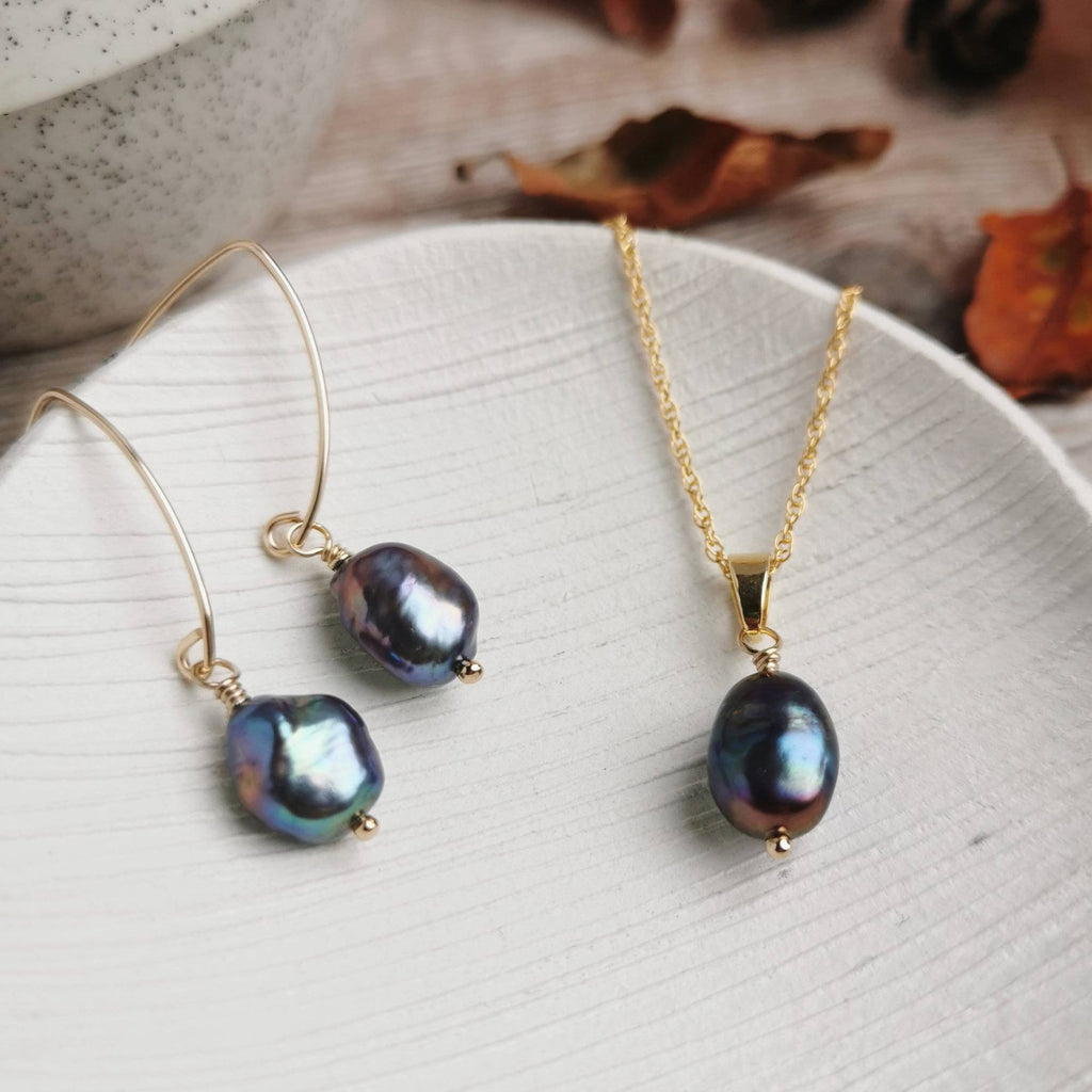 peacock purple baroque Pearl and gold necklace and matching earrings on a white ceramic dish with a blurred background