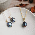 peacock purple baroque Pearl and gold necklace and matching earrings on a white ceramic dish with a blurred background