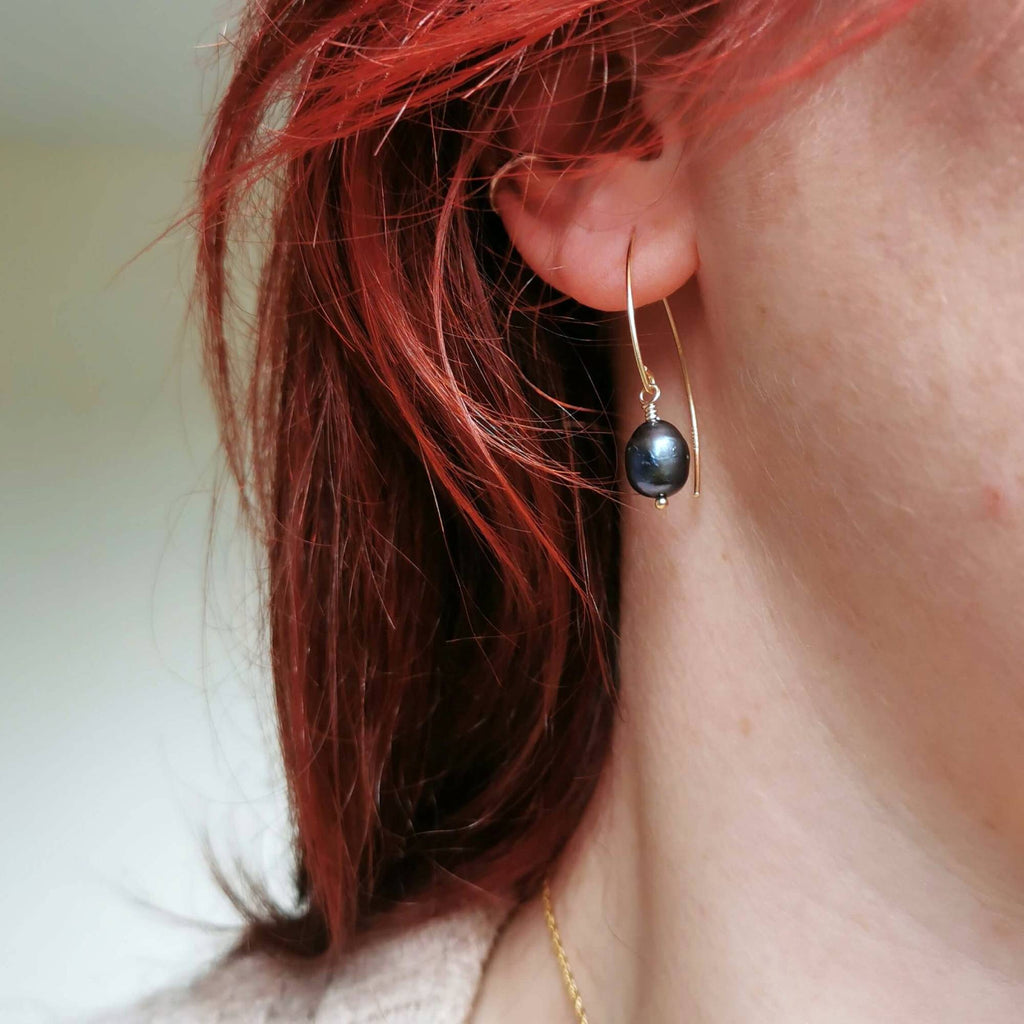 Close-up of a person wearing a black pearl and gold earrings