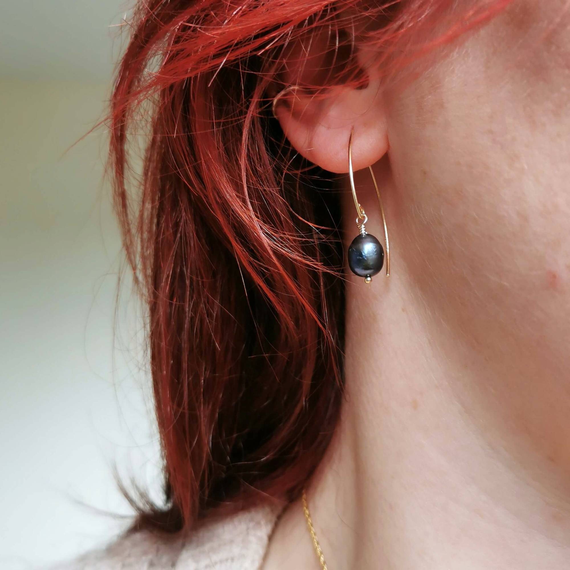 Close-up of a person wearing a black pearl and gold earrings