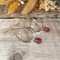 Textured Silver earrings with pink carved tourmaline leaf drops on a wooden surface with dried flowers.