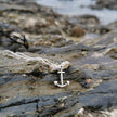 Silver anchor pendant on a chain lying on a rocky surface near the sea on the south coast of cornwall