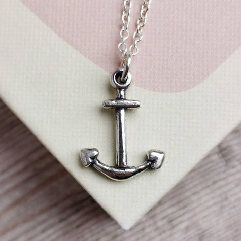 close up of a handmade silver anchor with silver chain on a pale pink and cream book cover