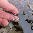 Silver anchor pendant held between fingers over a rockpool in cornwall, uk