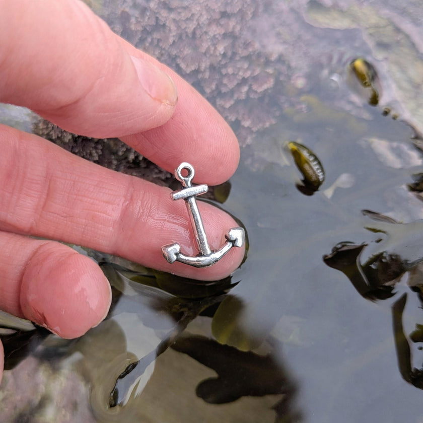 Silver anchor pendant held between fingers over a rockpool in cornwall, uk