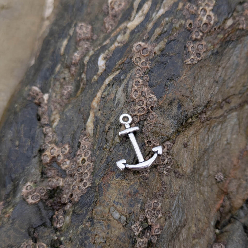 Silver anchor charm on textured stone with barnacles near rockpools in falmouth, cornwall