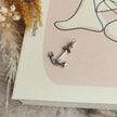 handmade silver anchor charm on a pale pink and cream book cover by Rupi Kaur