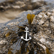 Silver anchor charm on seaweed with a rocky background by the sea in cornwall, uk