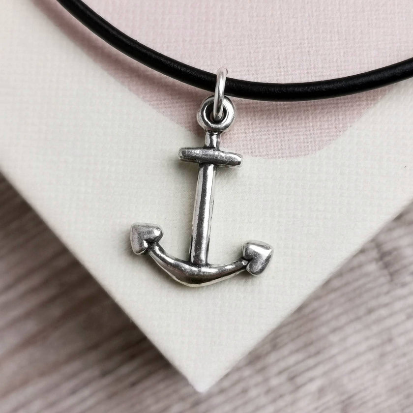 anchor pendant with a leather cord placed on a pale pink and cream book cover