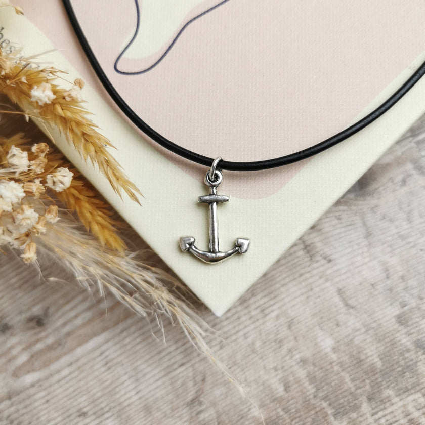 silver anchor pendant on a black leather cord, placed on a pink and cream book with dried flowers