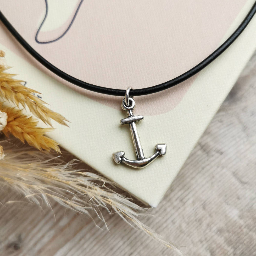 silver anchor necklace on a black cord positioned on top of a book with dried grasses